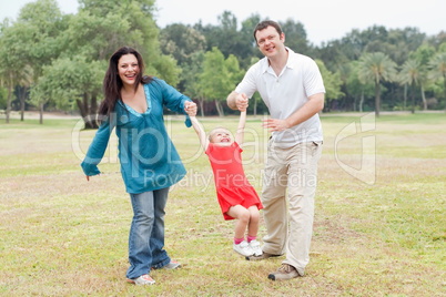 Happy couple playing on the green park with their beautiful daughter