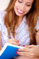 Young woman sitting on sofa writing in notepad