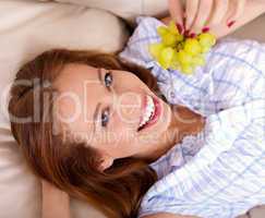 Happy young woman lying on sofa holding grapes