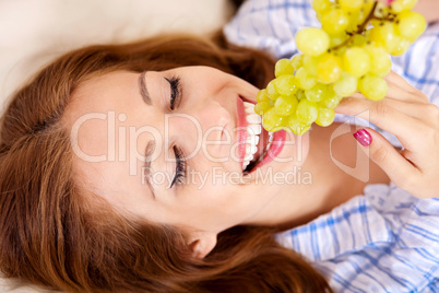 Happy young woman eating grapes