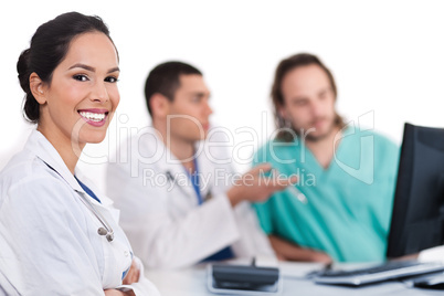 Smiling young doctor with other doctors behind her