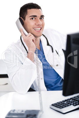 Smiling young physician sitting at his desk talking over phone