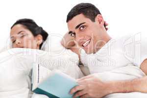 Woman sleeping and man happily reading book in bed