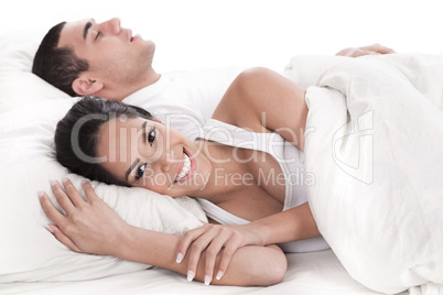 Couple lying in bed together, man sleeping and woman smiling