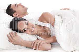 Couple lying in bed together, man sleeping and woman smiling