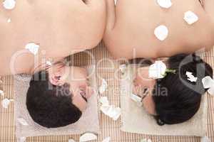 Portrait of fresh and beautiful man and woman lying around flowers and taking spa treatment