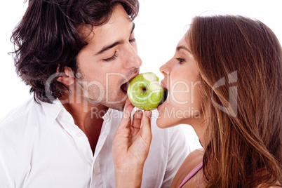 young couple playfully biting green apple