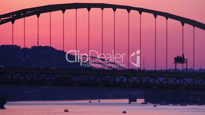 Traffic passes over the Fort Pitt Bridge during dusk in Pittsburgh, PA as pleasure boats travel underneath.