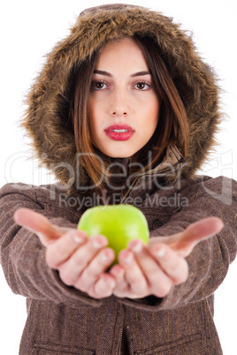 Beautiful young lady showing green apple wearing a fur coat with