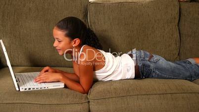 A young girl uses her laptop on the sofa.