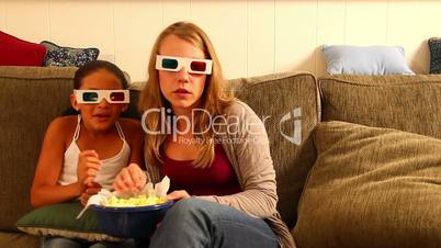 A young girl and woman watch a scary 3D movie with popcorn.