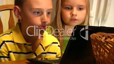 Young children use a laptop in the kitchen.