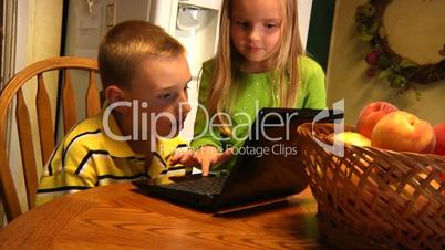 Young children use a laptop in the kitchen.