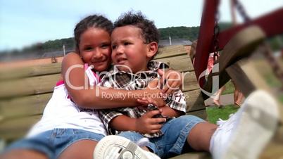 A brother and sister hug on a swing.