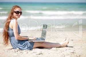 Woman working on a laptop by sitting on the beach