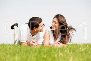 young couple smiling by laying down in a green grass field