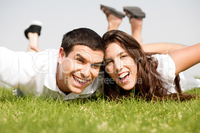 Playful young couple laying down in a green grass field