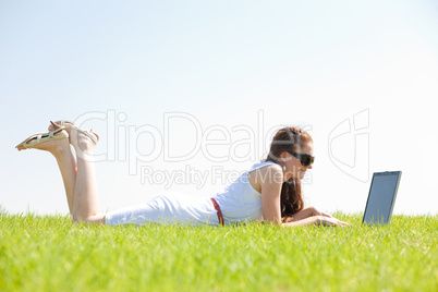 oung female lying on the grass in the park using a laptop