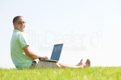 A young men sit on the in the park using a laptop