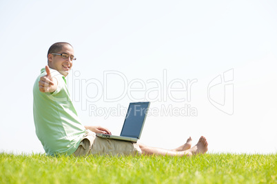 A young men sit on the in the park using a laptop