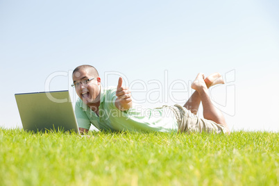 A young men sit on the in the park using a laptop