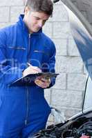 Handsome mechanic writing on a clipboard standing in front of a