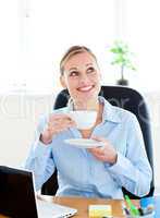 Delighted businesswoman drinking coffee in front of her laptop i