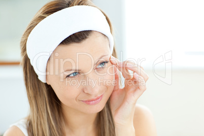 Pretty woman putting cream on her face wearing a headband in the
