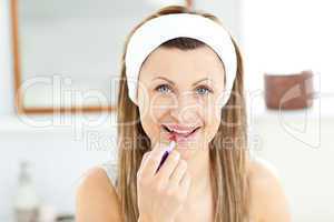 Delighted young woman using a red lipstick in the bathroom