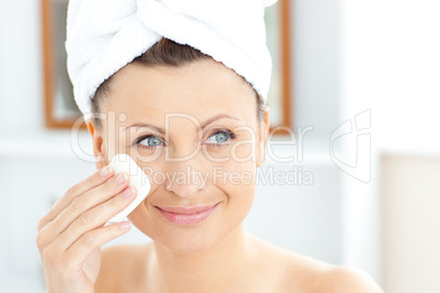 Young woman putting cream on her face wearing a towel in the bat
