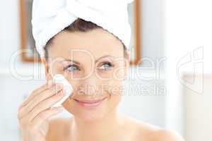 Young woman putting cream on her face wearing a towel in the bat