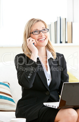 Serious businesswoman talking on phone and using her laptop sitt