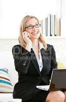 Serious businesswoman talking on phone and using her laptop sitt
