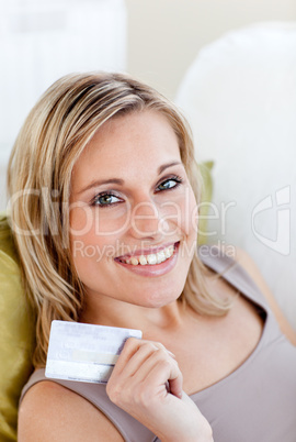 Cheerful caucasian woman holding a card sitting on a sofa in the