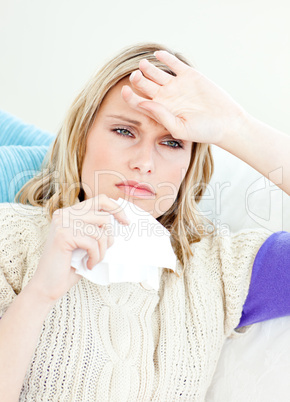 Ill woman holding a tissue sitting on a sofa