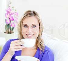 Charming woman enjoying her coffee sitting on a sofa in the livi