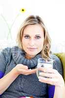 Sick woman taking pills holding a glass of water sitting on a so