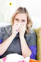 Sick woman using a tissue sitting on a sofa