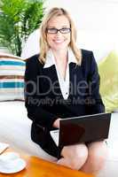Merry businesswoman with glasses using her laptop on a sofa