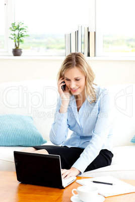 Busy businesswoman using her laptop and her cellphone at home