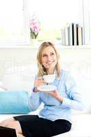 Smiling businesswoman holding a cup of coffee sitting on a sofa