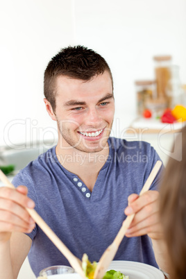 Happy man putting salad on a plate having dinner with his girlfr