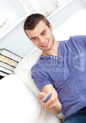 Serious young man holding a remote sitting on the sofa in the li