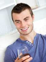 Handsome young man holding a glass of wine sitting on a sofa in