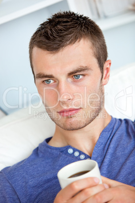 Charming caucasian man holding a cup of coffee in the living-roo