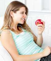 Happy young woman holding an apple on a sofa