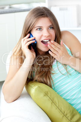 Surprised woman talking on phone lying on a sofa in the living-r
