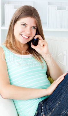 Joyful young woman talking on phone sitting on a sofa