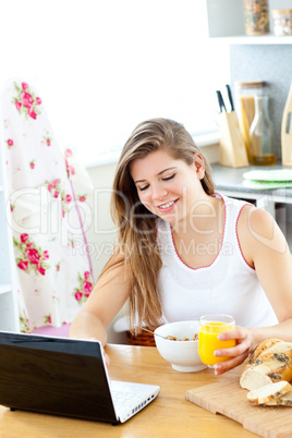 Enthusiastic young woman using her laptop while having breakfast