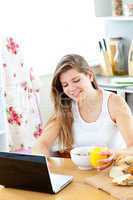 Enthusiastic young woman using her laptop while having breakfast